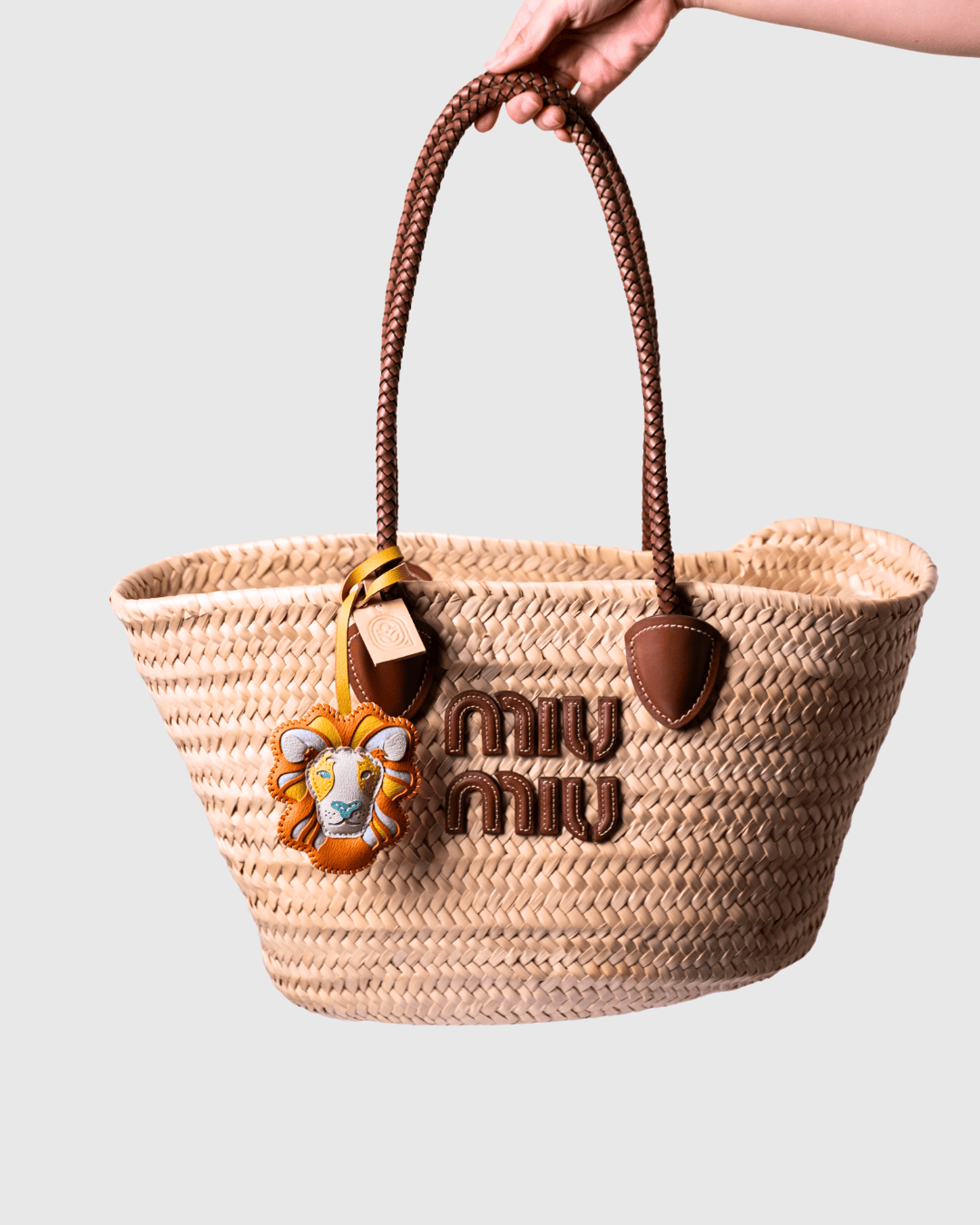 Straw tote bag with brown leather handles and lion charm.