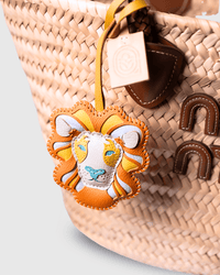 Lion-shaped leather bag charm on a woven basket.