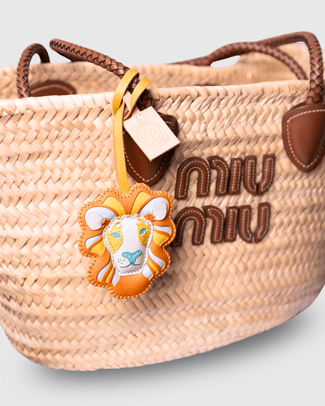 Woven straw handbag with leather lion charm.