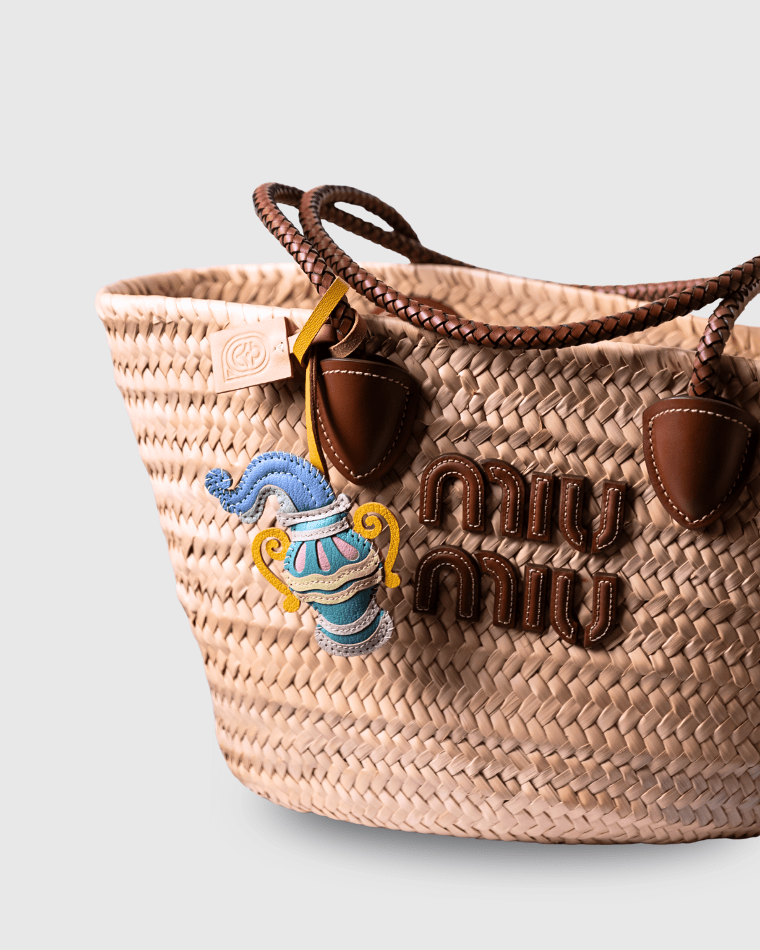 Woven straw tote bag with brown leather handles and charm.