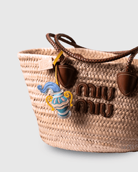 Woven straw tote bag with brown leather handles and charm.
