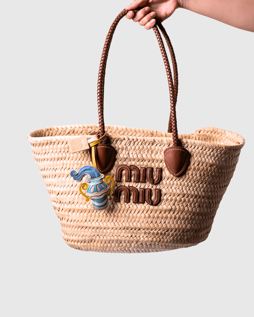 Woven straw tote bag with brown leather handles and logo.