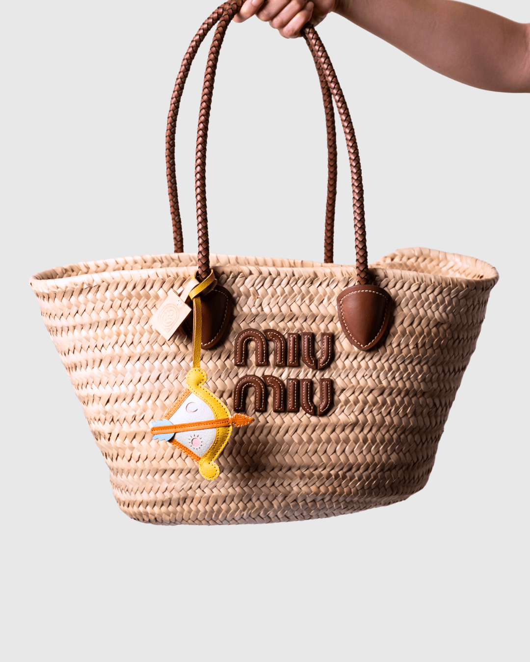 Straw tote bag with brown handles and logo.