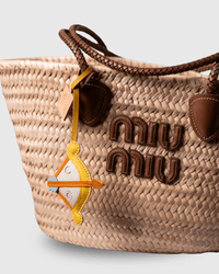 Woven straw tote bag with brown leather accents and a decorative charm.