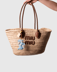 Hand holding a woven straw tote bag.