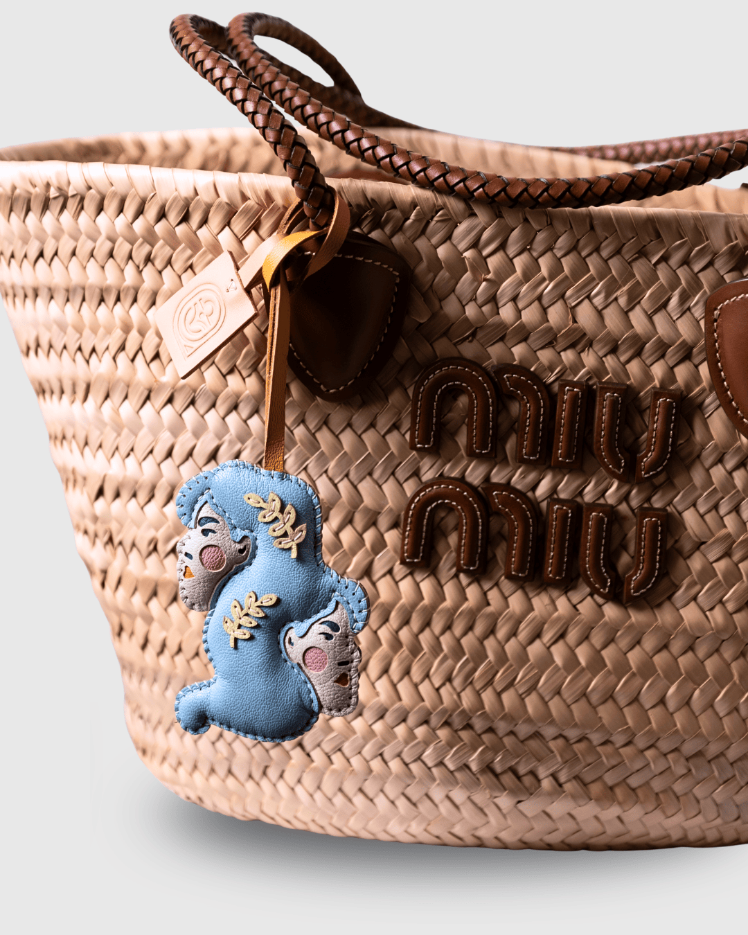 Woven straw handbag with leather accents and charm.