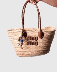Woven straw tote bag with brown leather handles and charm.