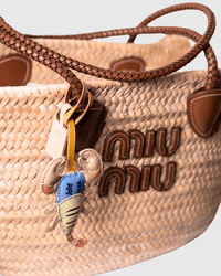 Woven handbag with leather handles and a lobster charm.