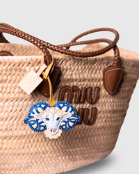 Woven straw tote bag with leather handles and decorative charm.