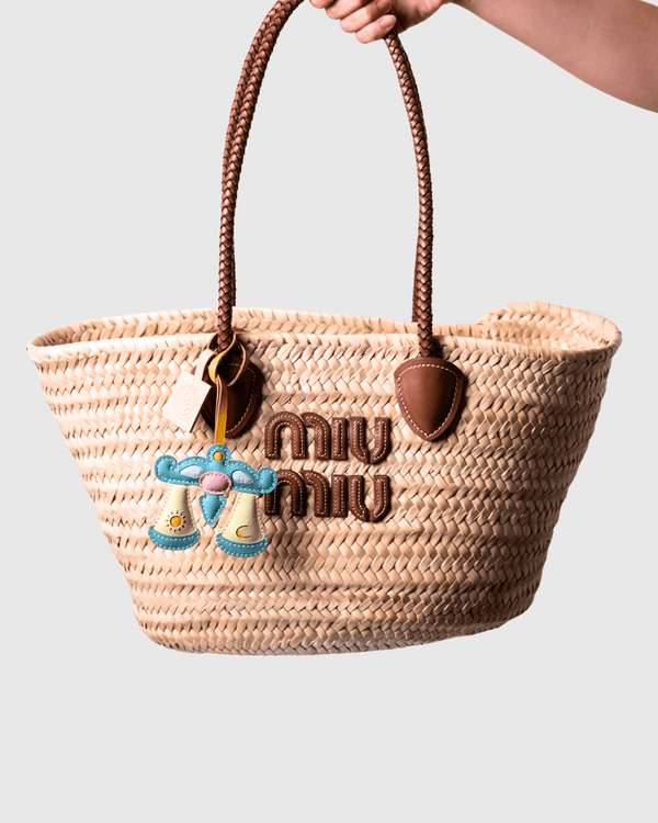 Woven straw tote bag with brown handles and logo.