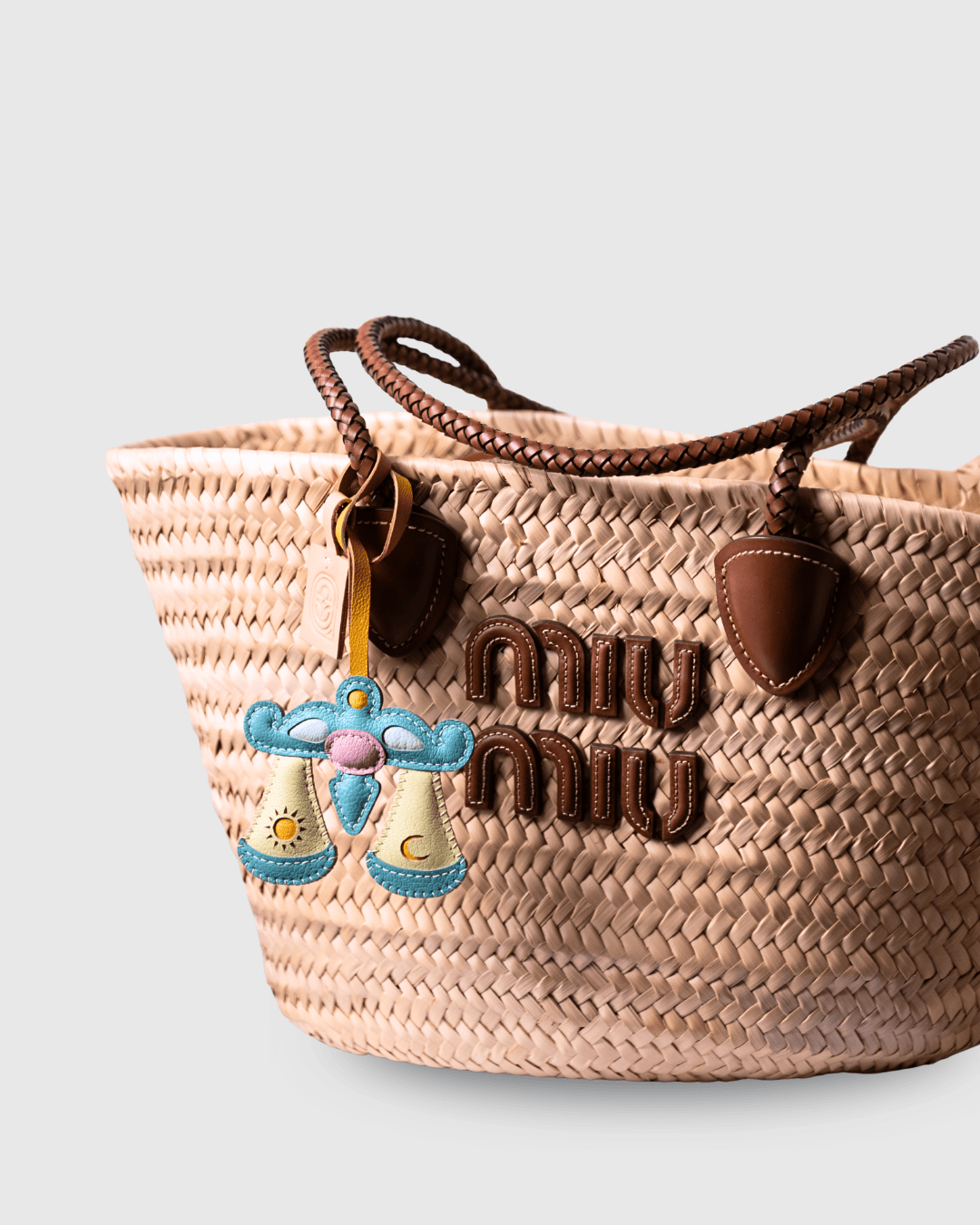 Woven straw handbag with leather handles and decorative charm.
