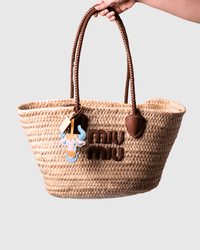 Woven straw tote bag with brown leather handles and logo.