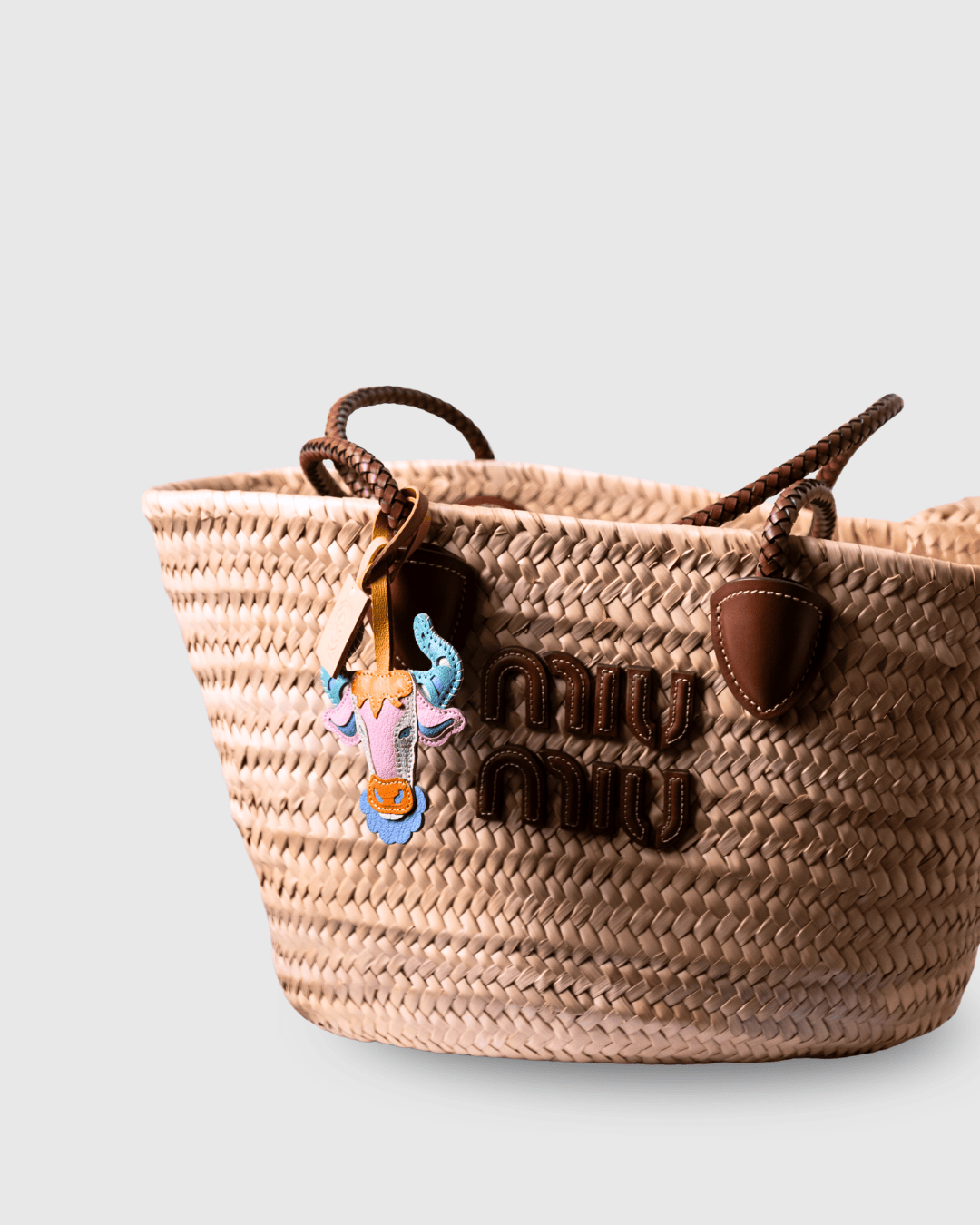 Woven tote bag with cow charm and miu miu logo.