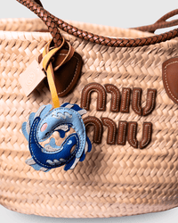Woven straw bag with leather accents and charm.