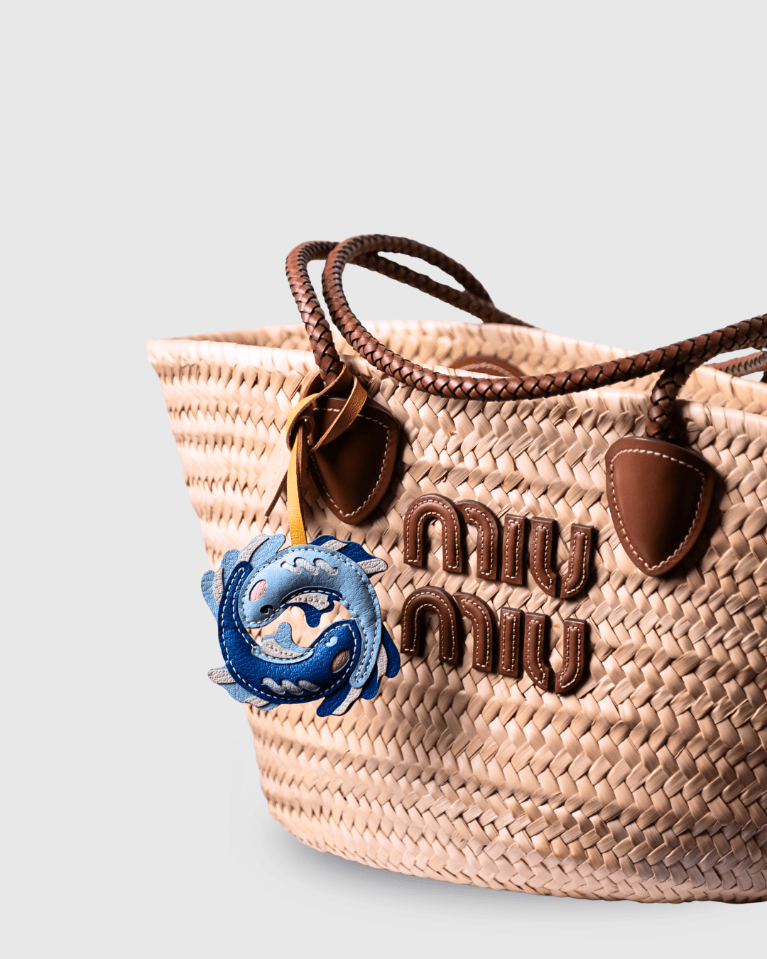 Straw tote bag with fish charm and brown leather accents.