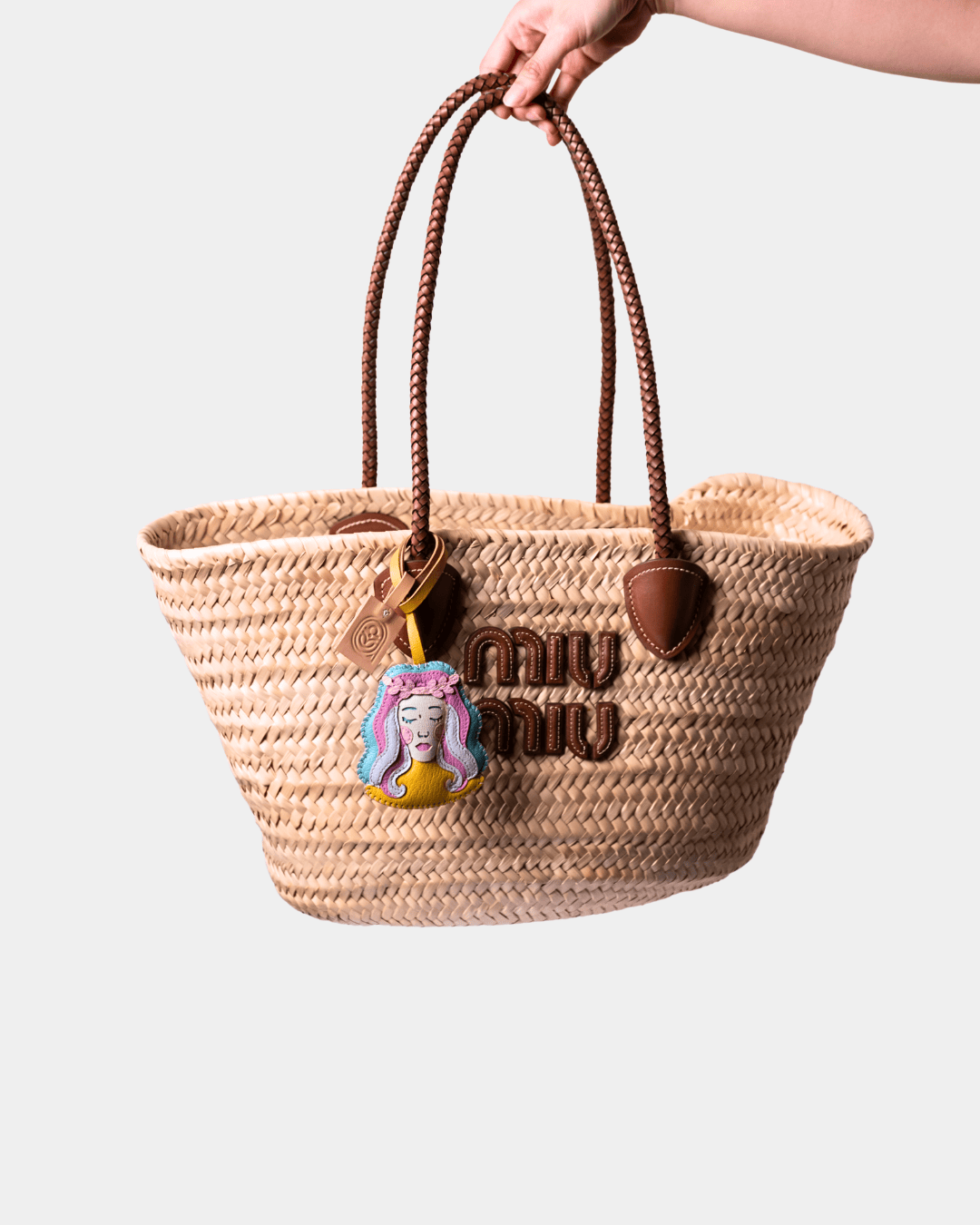 Woven straw tote bag with brown leather handles and charm.