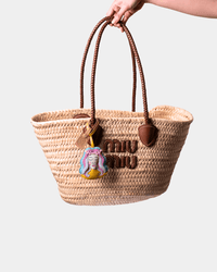 Woven straw tote bag with brown leather handles and charm.