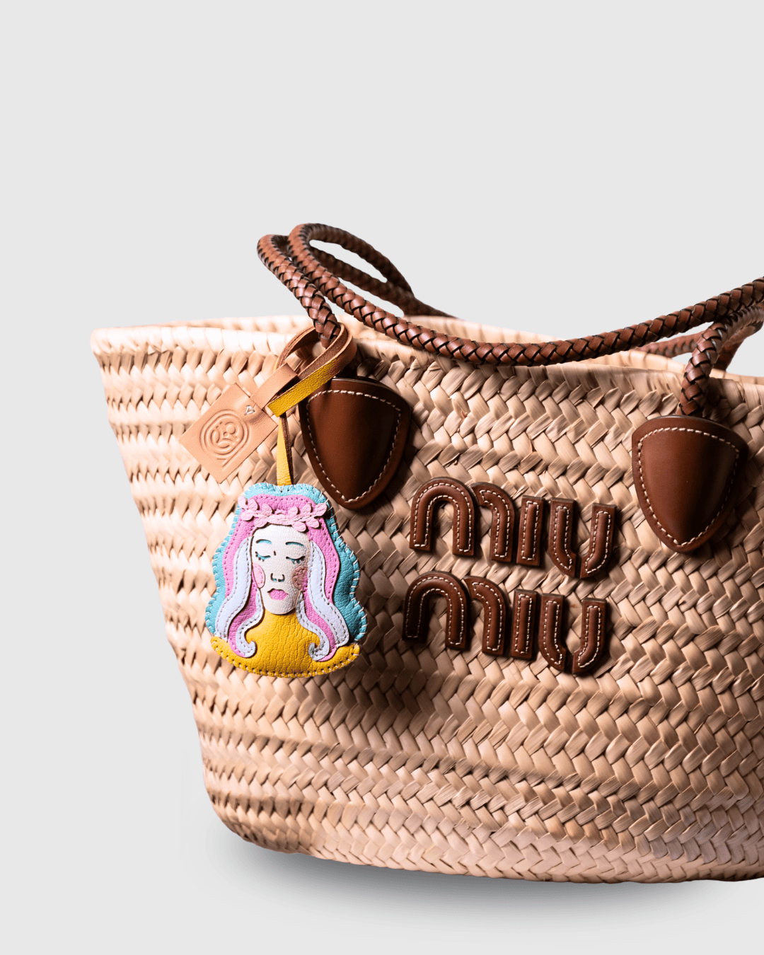 Straw tote bag with charm and logo detail.