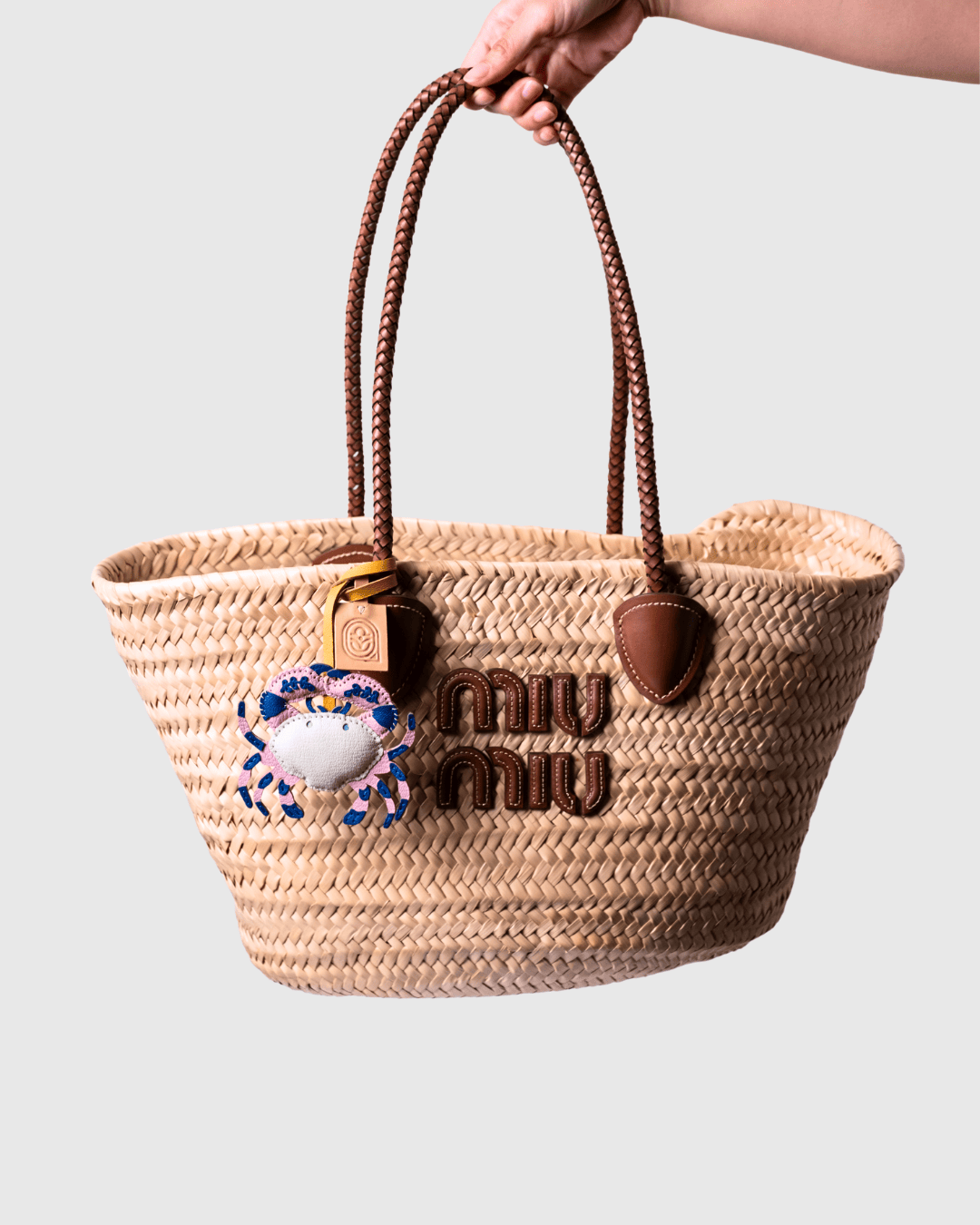 Woven straw tote bag with brown leather handles and charm.