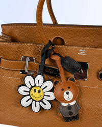Hermes brown leather handbag with a flower and bear keychain leather charm on a light blue background