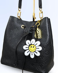 Black textured handbag with a white daisy charm on a light blue background