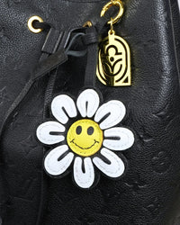 Smiley face flower leather bag charm attached to a black bag with a gold hook.