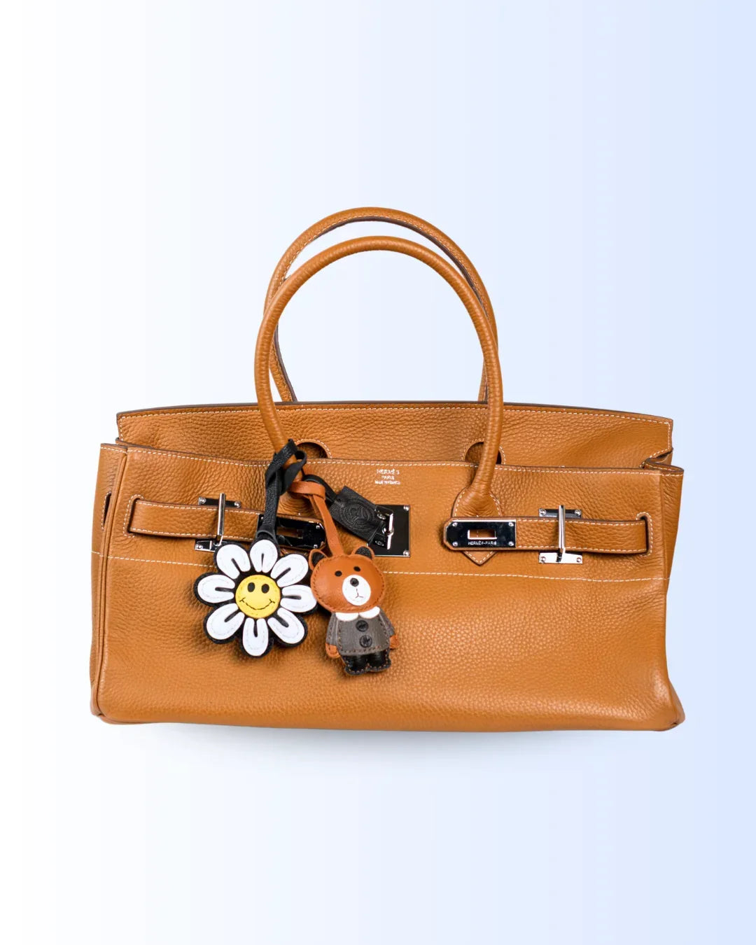 Brown handbag with a flower and bear keychain leather charms on a light blue background