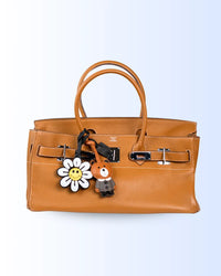 Brown handbag with a flower and bear keychain leather charms on a light blue background