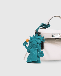 Teal Statue of Liberty keychain attached to a white bag on a light gray background