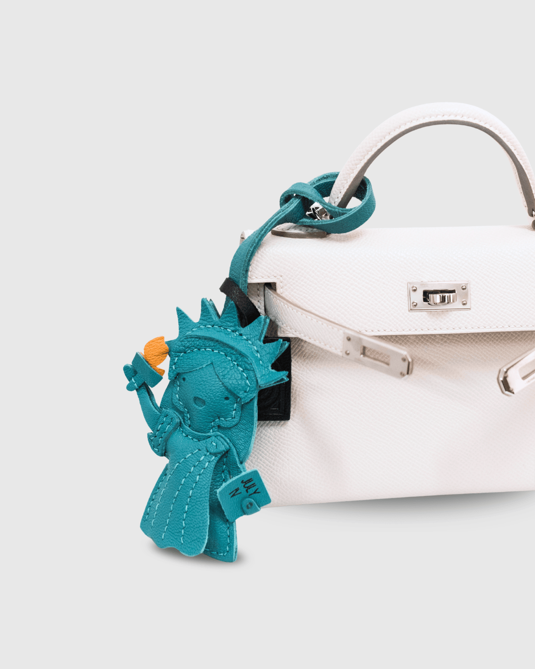 Turquoise Statue of Liberty keychain attached to a white handbag on a light gray background