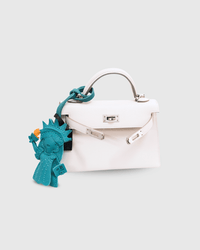 White handbag with a blue charm featuring a stylized figure on a light gray background