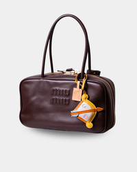 A dark brown leather Miu Miu handbag with gold-tone hardware, featuring the embossed 'miu miu' logo on the front and a decorative yellow and white patchwork charm.