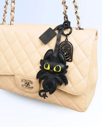 Beige quilted chanel handbag with a black dragon charm on a light blue background