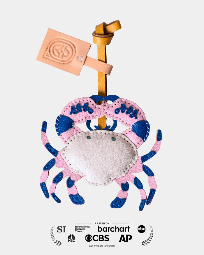 leather crab with a pink shell and blue accents, holding a sign, on a white background.