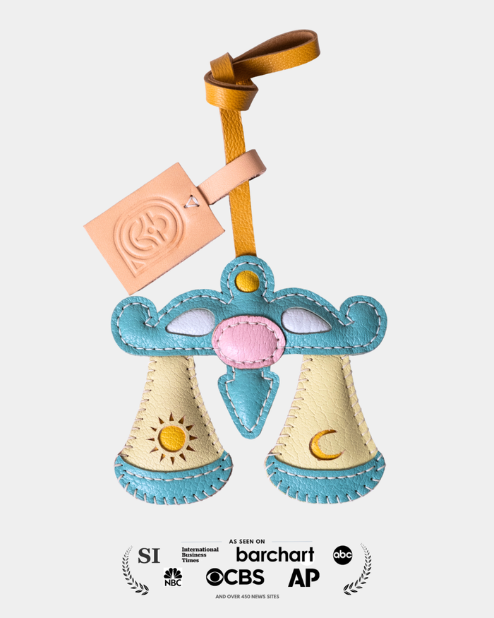 leather product in a scale shape representing libra horoscope and a strap on a light gray background
