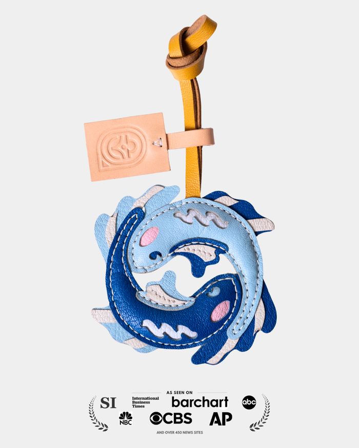 blue double fish-shaped leather charm with a gold handle on a white background