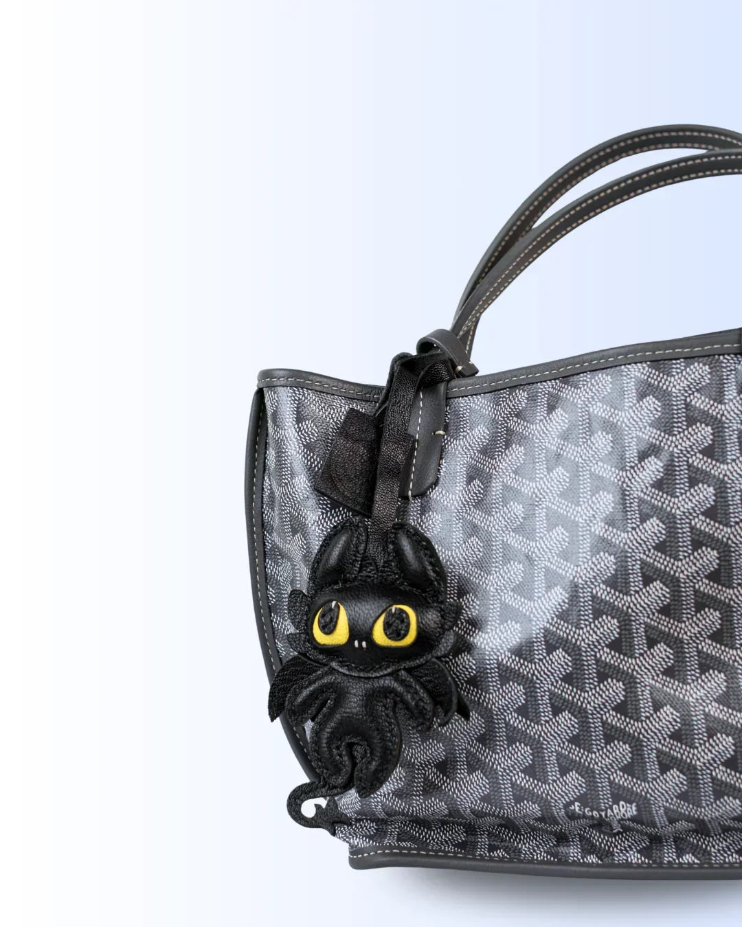 Black dragon leather bag charm on a patterned handbag against a light blue background